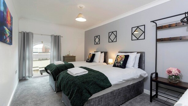 A modern bedroom with a large bed, two bedside tables, a bench, and a view of the city.