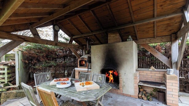 Un patio al aire libre con un horno de ladrillo, una mesa y sillas de madera.