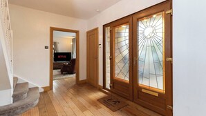 Un pasillo con suelo de madera, una escalera y una puerta con un diseño de vitral.