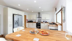 Una cocina moderna con armarios blancos, una mesa de comedor de madera y una campana extractora de acero inoxidable.