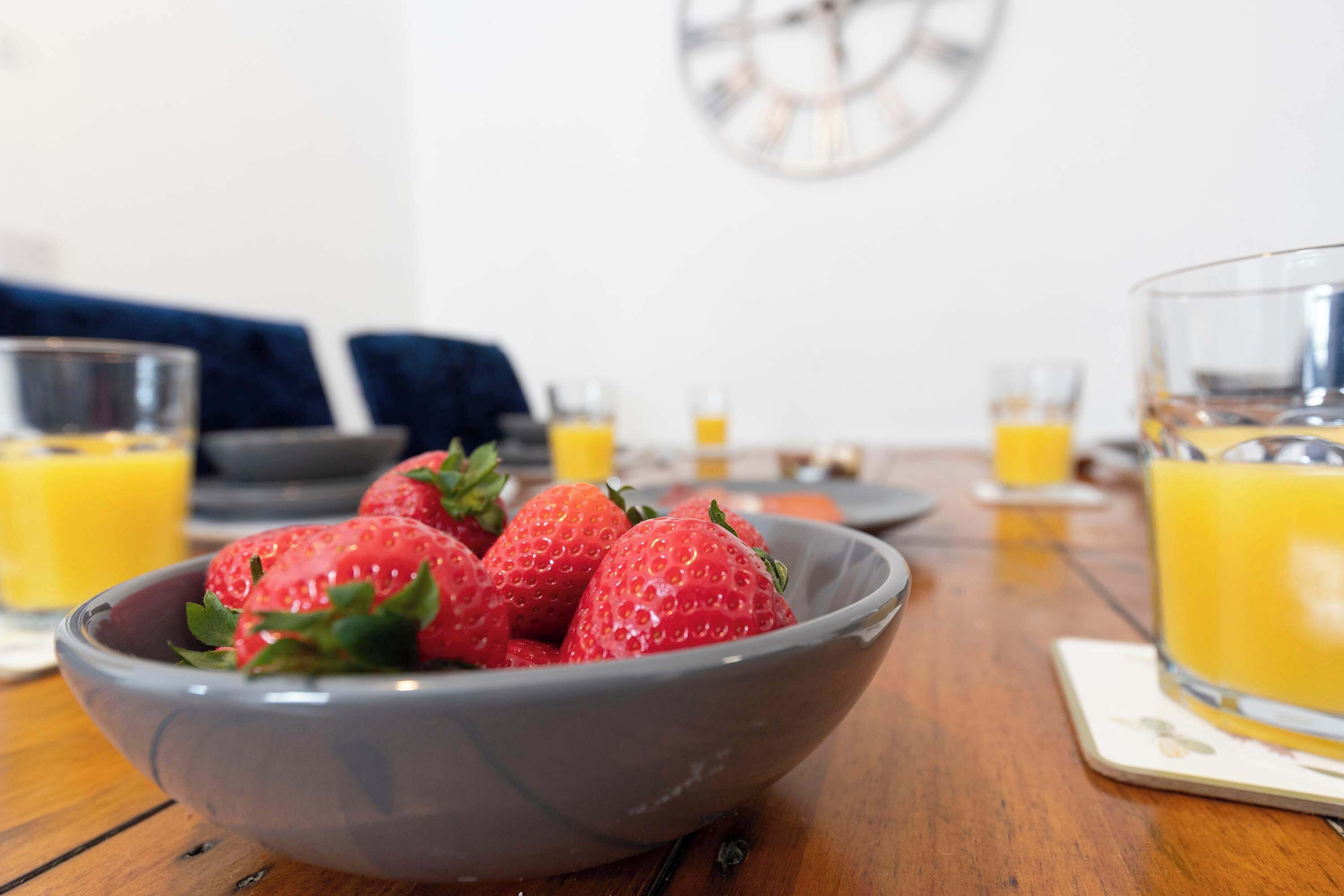 Een schaal verse aardbeien op een houten tafel met glazen sinaasappelsap.