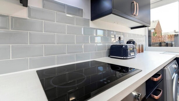 A modern kitchen with grey tiled backsplash, black cabinets, and stainless steel appliances. - Spacious 3 Bedroom Home in Guisborough (Redcar and Cleveland)