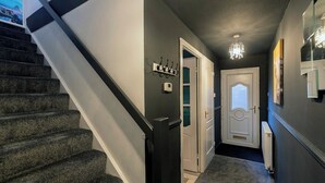 Um corredor com escada revestida de carpete, porta com painel de vidro, luminária fixada na parede e radiador.