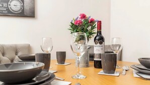 Uma mesa de jantar posta com pratos, tigelas, copos e talheres. Há também uma garrafa de vinho e um vaso com flores à vista.
