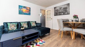 Uma sala de estar moderna com um sofá azul escuro, uma mesa de jantar de madeira e um quadro abstrato vibrante.