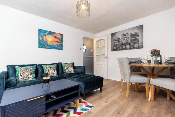A modern living room with a dark blue sofa, a wooden dining table, and a vibrant abstract painting. - In the heart of it! S (Stokesley)