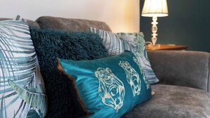 Ein graues Sofa mit einem türkisfarbenen Kissen mit Bär-Motiv, einer flauschigen, türkisfarbenen Decke und einer Lampe auf einem Holznachttisch.