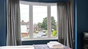 Ein Schlafzimmer mit einem großen Fenster, einem Bett mit farbenfroher Decke und einem ordentlich bezogenen Bett mit Handtüchern.