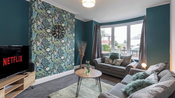 Ein Wohnzimmer mit großem Flachbildfernseher, einer Sofagarnitur, einem Couchtisch und einer Wand mit floralem Dekor.