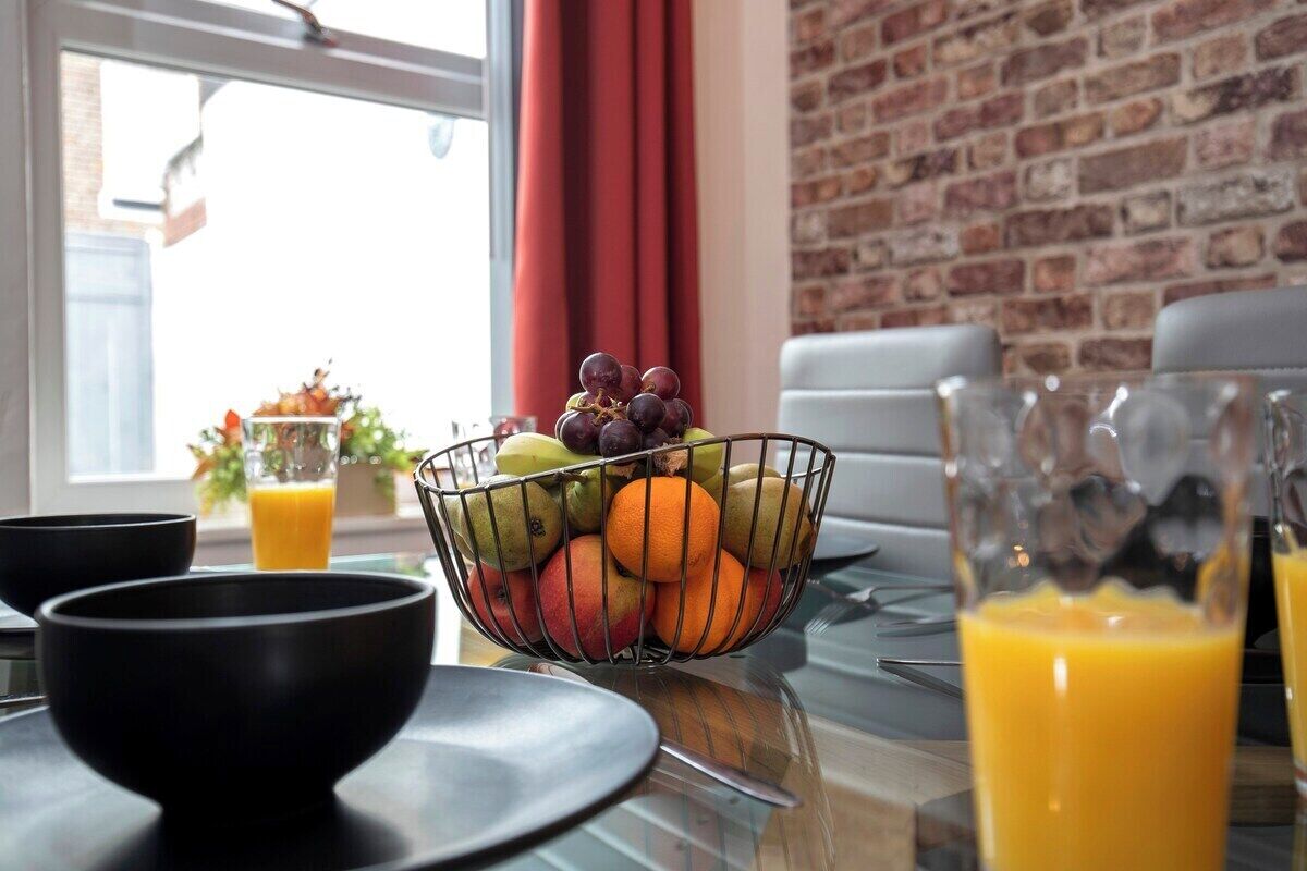 A breakfast setting with a fruit bowl, black bowls, and glasses of orange juice on a table.