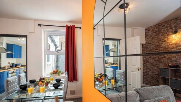 Ein modernes Wohnzimmer mit einem Glastisch, einem grauen Sofa und orangefarbenen Akzenten.