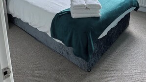Una cama bien tendida con almohadas blancas y amarillas, una manta color turquesa y toallas blancas dobladas.