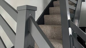 Una escalera con barandilla gris y alfombra estampada, que lleva a un rellano con cuadros en la pared.