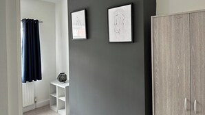 Un pasillo con una pared gris oscuro, un estante blanco con un reloj y un armario.