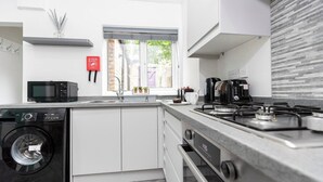 A modern kitchen with a washing machine, microwave, stove, and sink. - The Normanby! Summary (Normanby)