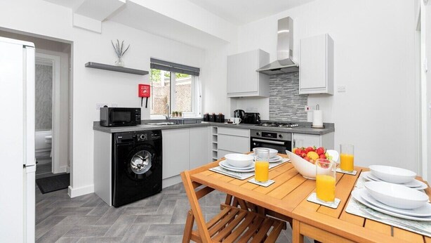 A modern kitchen with a dining area, including a washing machine, microwave, and a table set with plates and glasses of orange juice. - The Normanby! Summary (Normanby)