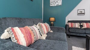 A modern living room with teal walls, a grey sofa, and a matching armchair. There are decorative pillows on the sofa and armchair, a floor lamp, and artwork on the walls. - The Normanby! Summary (Normanby)