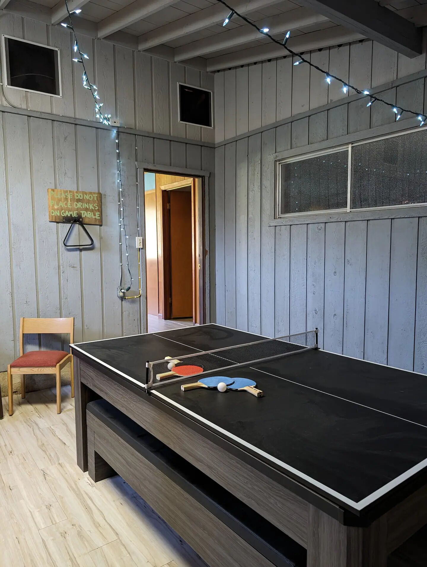 A ping pong table in a room with wooden walls, a chair, and a sign instructing not to place drinks on the table.
