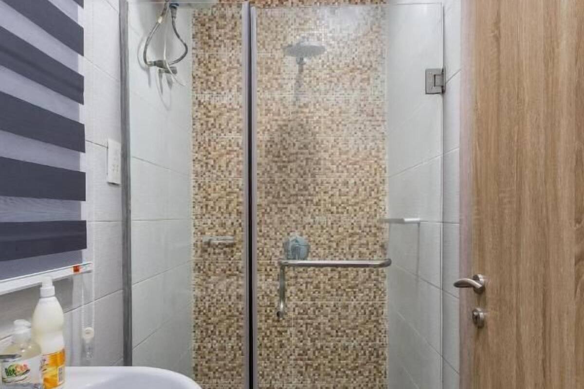 A bathroom with a glass shower enclosure, a white sink, and a wooden door.