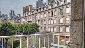Een balkon met een tafel, een theepot en een mok. Het balkon heeft uitzicht op een rij historische gebouwen met stenen gevels en meerdere ramen en balkons.