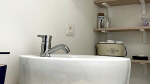 Une salle de bain avec un lavabo blanc, un miroir rond et un meuble de rangement portant l’inscription « RANGEMENT SALLE DE BAINS ».