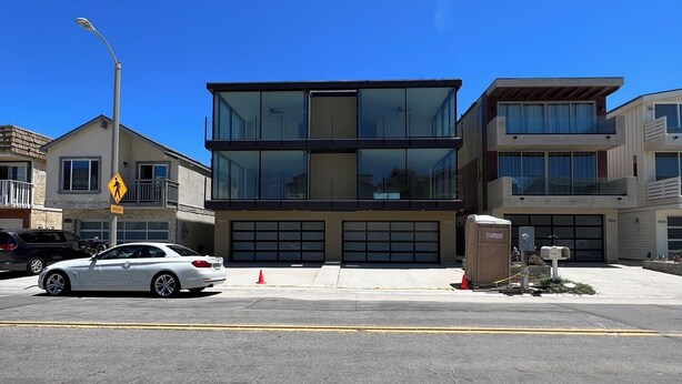 Un bâtiment moderne avec une entrée de garage, une rue où se trouve une voiture blanche et un panneau de passage piéton.