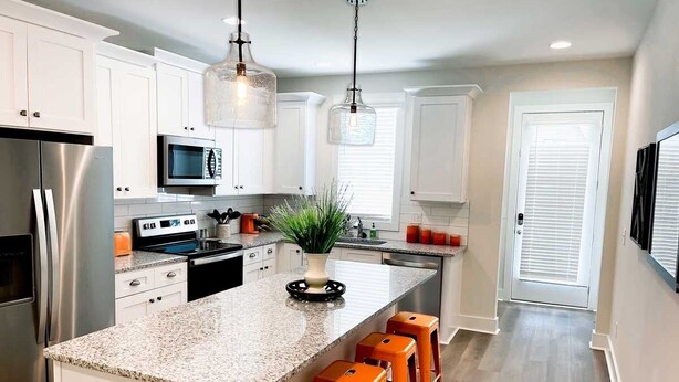 A modern kitchen with white cabinets, stainless steel appliances, a granite countertop, and orange bar stools. - Aubie’s Favorite Place near Campus and Tiger Town with 2 King & 2 Queen beds  (Auburn)