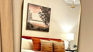 A bedroom with a bed, pillows, a bedside lamp, a painting, and a mirror. - Aubie’s Favorite Place near Campus and Tiger Town with 2 King & 2 Queen beds  (Auburn)