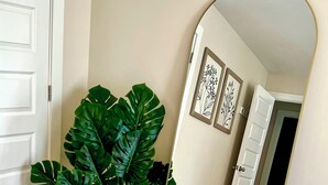 A room with a large mirror reflecting a patterned rug, a potted plant, and a door. - Aubie’s Favorite Place near Campus and Tiger Town with 2 King & 2 Queen beds  (Auburn)