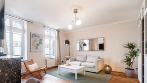 Een moderne woonkamer met een witte bank, een bijzettafeltje, een rieten fauteuil en een potplant.