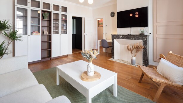 Een moderne woonkamer met een witte bank, een salontafel, een open haard en een televisie die aan de muur is bevestigd.