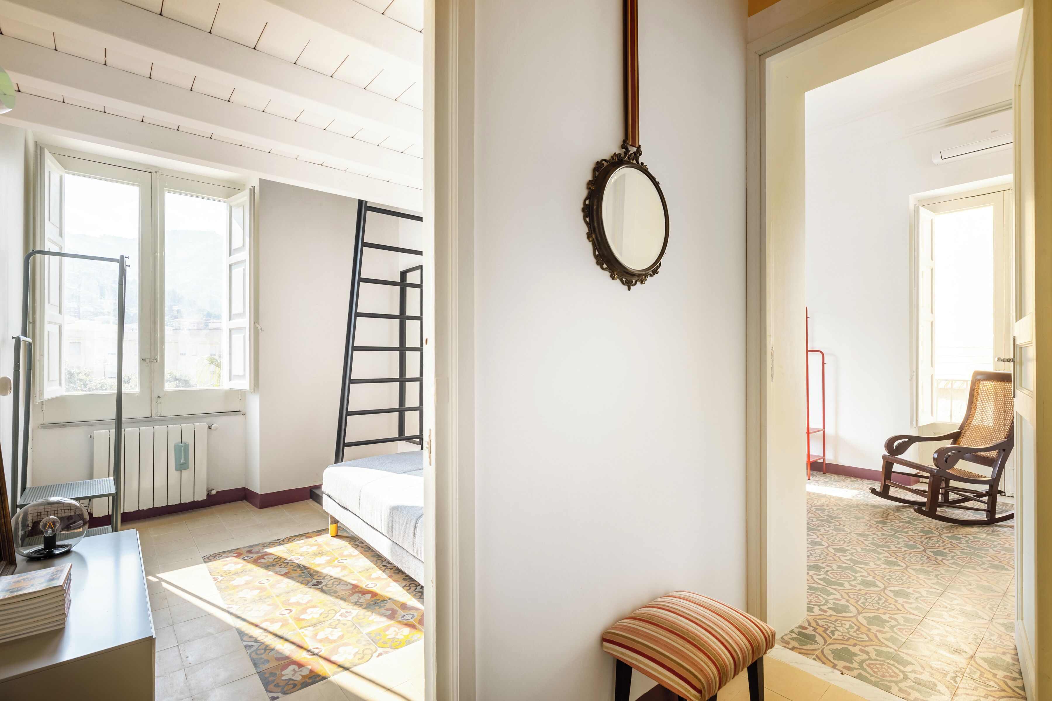 A room with a bed, a chair, a mirror, and a window.