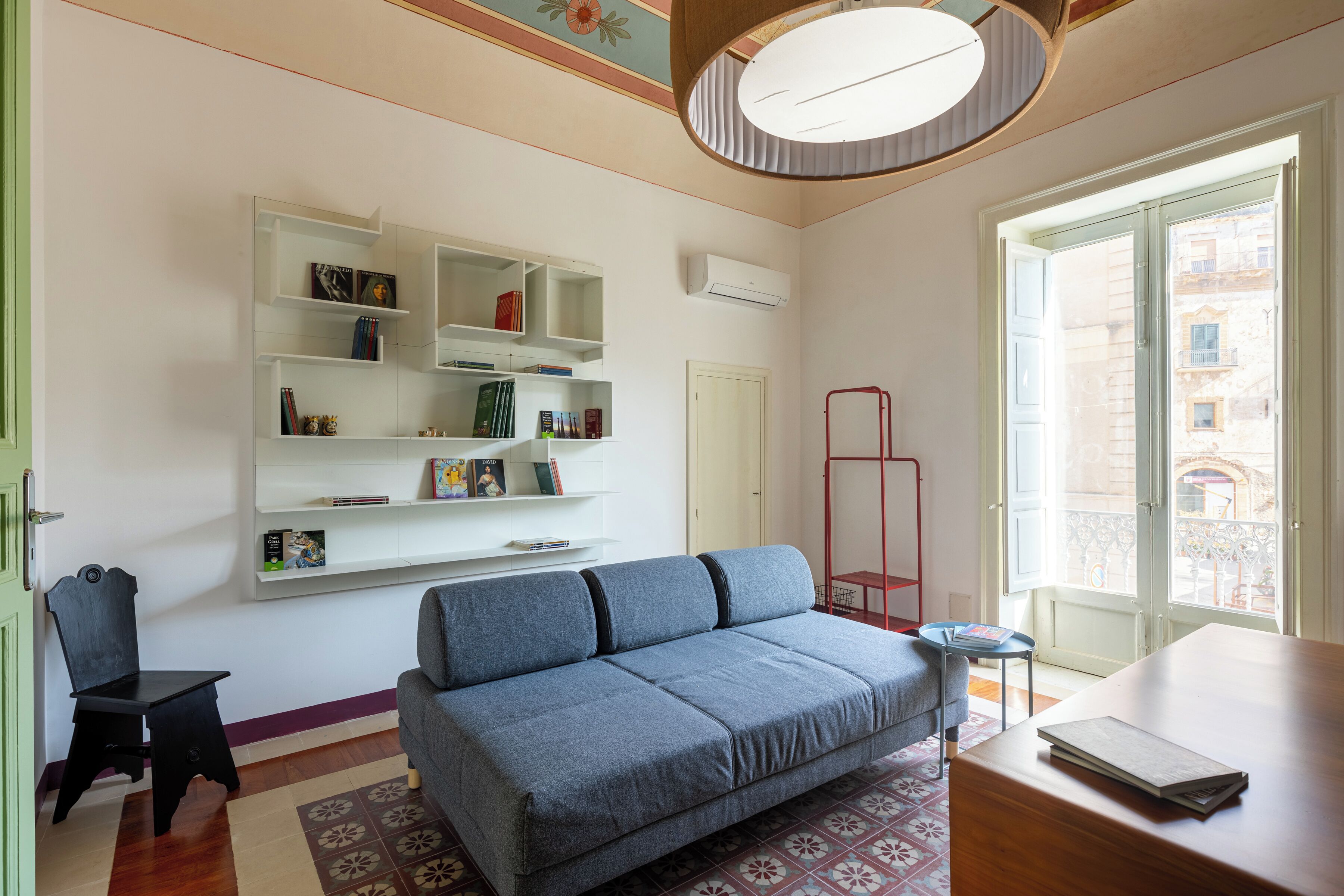 A living room with a sofa, a small table, a bookshelf, and a window with a view of buildings.