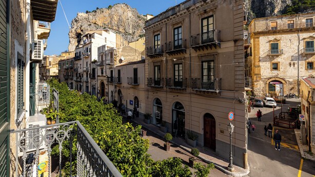A narrow street lined with historic buildings, balconies, and a rocky cliff in the background. - Eleganza in Centro a Cefalù by Wonderful Italy (Cefalù)