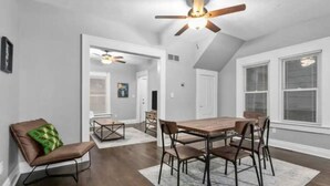 A dining area with a wooden table and chairs, a ceiling fan, and a view of the adjacent room. - Experience KC from Twin Bells: Two Charming Bungalows, One Prime Location! (Kansas City)