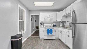 A modern kitchen with white cabinets, a stainless steel refrigerator, and a built-in oven. - Experience KC from Twin Bells: Two Charming Bungalows, One Prime Location! (Kansas City)