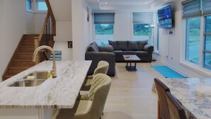 Eine moderne Küche mit Marmorarbeitsplatte und integriertem Spülbecken, ein Wohnbereich mit grauem Sofa und Couchtisch sowie eine Treppe zu einer oberen Ebene.