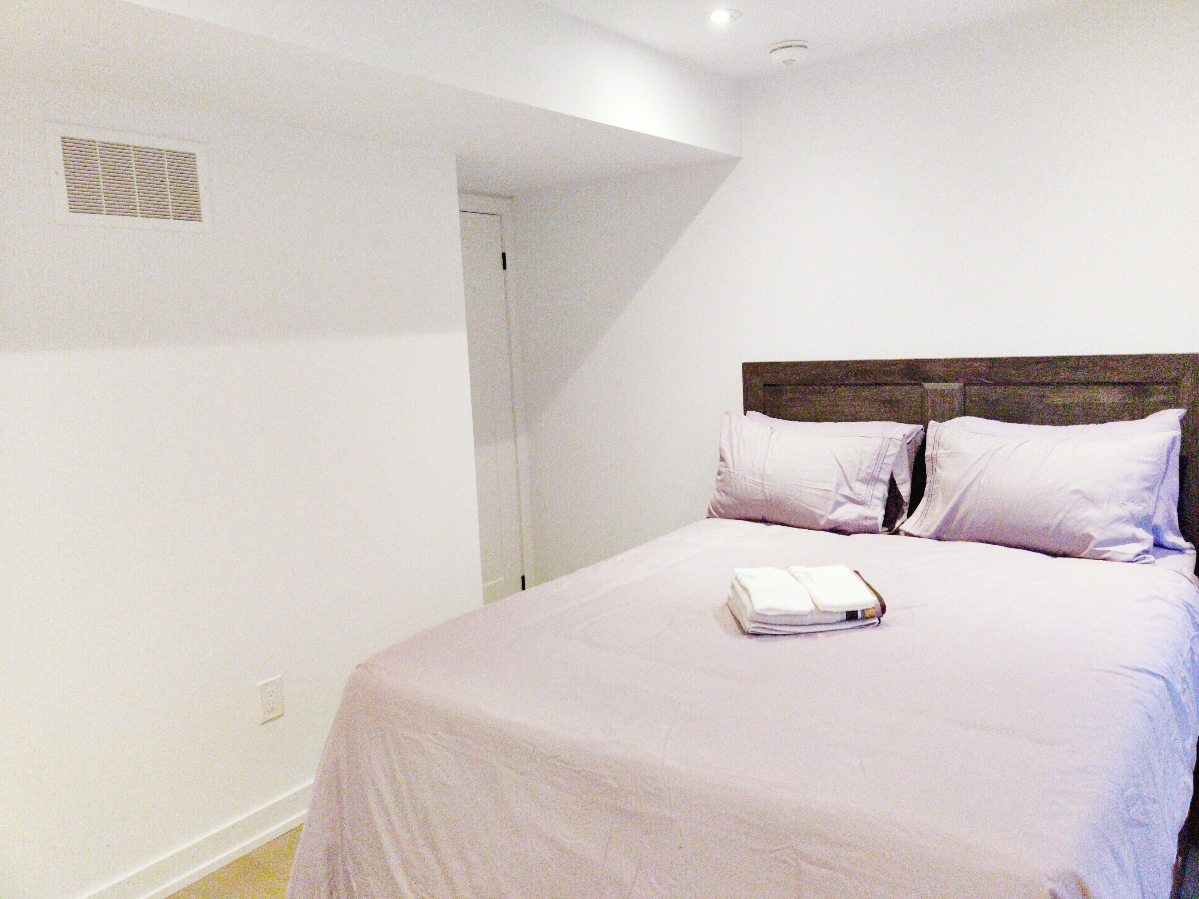 Cama bem arrumada com cobertura branca, cabeceira de madeira e duas almofadas.