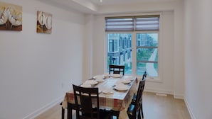 Ein Essbereich mit einem Tisch für vier Personen, einem großen Fenster mit Jalousien und zwei an der Wand hängenden Bildern.