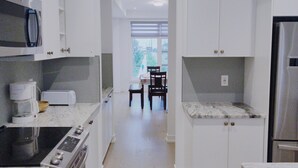 Eine moderne Küche mit weißen Schränken, einem eingebauten Ofen und einem Edelstahl-Kühlschrank. Im Hintergrund befindet sich ein Essbereich mit Tisch und Stühlen.