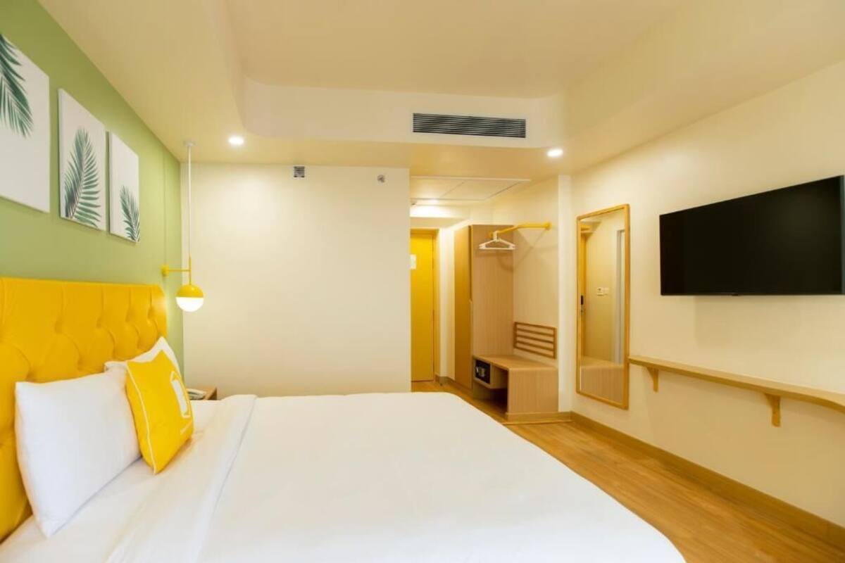 Una camera d'albergo con un letto, una TV, uno specchio e un corridoio che porta al bagno.