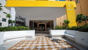 A hotel entrance with a checkered floor, a yellow sign listing amenities, and a modern building facade. - Bloom Hub - Guindy (Chennai)