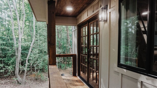 Une terrasse en bois avec une porte vitrée donnant sur une zone boisée.