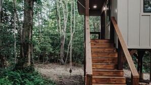 Un escalier en bois mène à une maison moderne entourée d’une forêt.