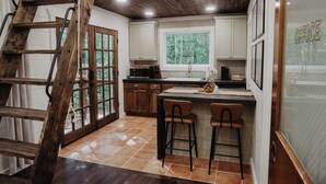 Une cuisine avec un escabeau en bois, des meubles blancs, une grande fenêtre et un coin bar.