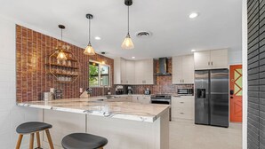 Una cocina moderna con una isla central, iluminación colgante y un refrigerador de acero inoxidable.
