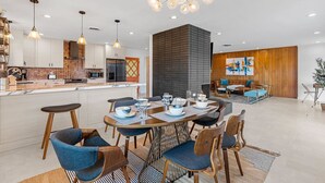 Cocina moderna con una isla central, iluminación colgante y un comedor con una mesa redonda y sillas.