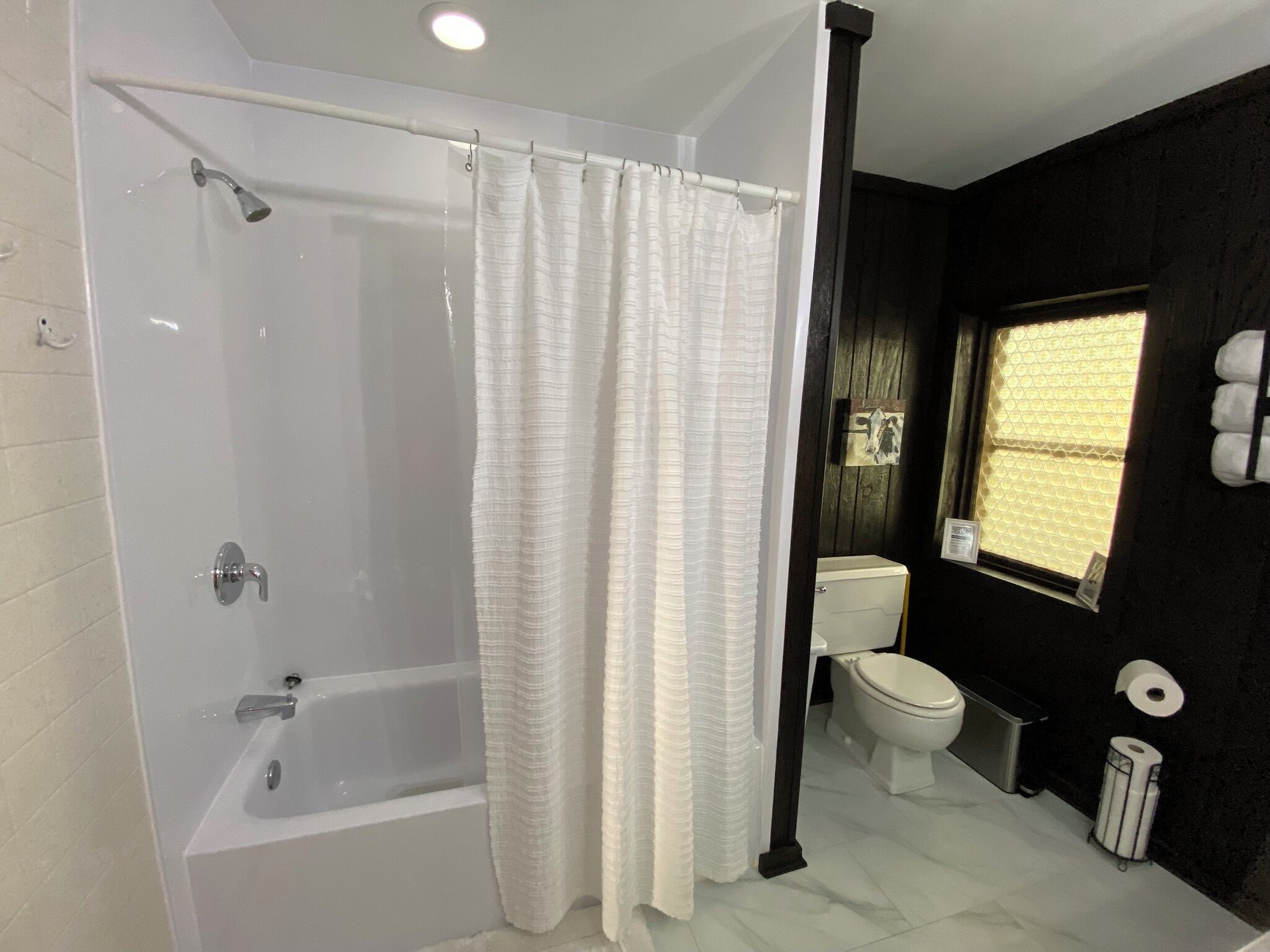 A bathroom with a bathtub, toilet, and a window with a towel rack.