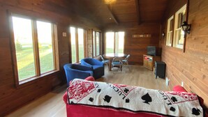 A cozy cabin interior with a wooden interior, a round dining table, blue chairs, and a red and white blanket on a couch. - Pet-friendly, Kid-friendly Farmhouse near Holy Hill, Ice Age Trail, State Forest (Hubertus)