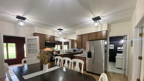 A modern kitchen with dark wooden cabinets, stainless steel appliances, and white chairs. - Pet-friendly, Kid-friendly Farmhouse near Holy Hill, Ice Age Trail, State Forest (Hubertus)